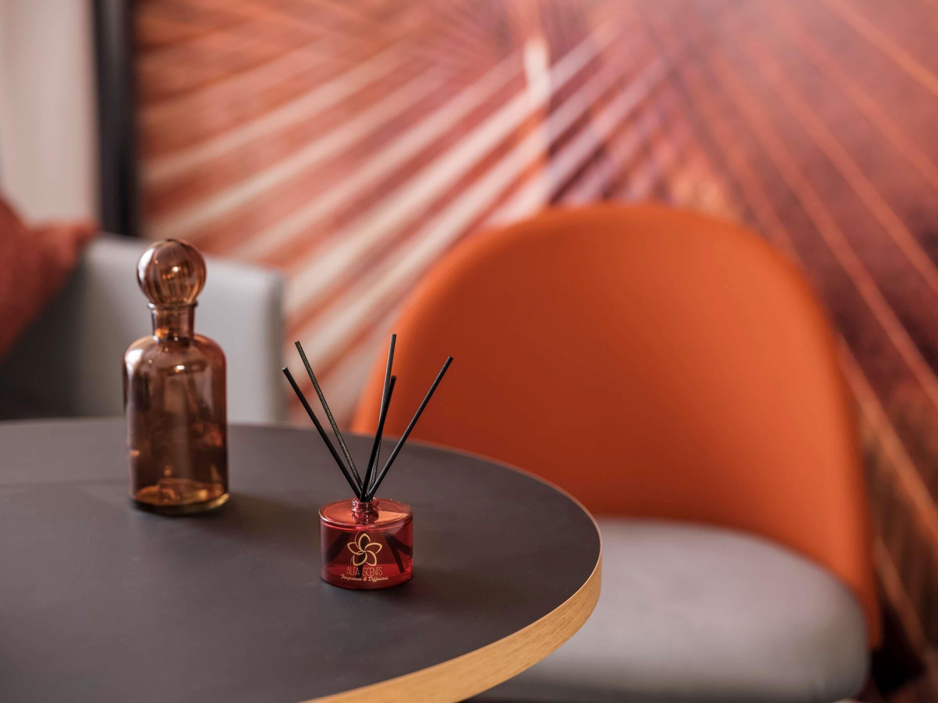 A round table with a red candle holder and a diffuser with black sticks.