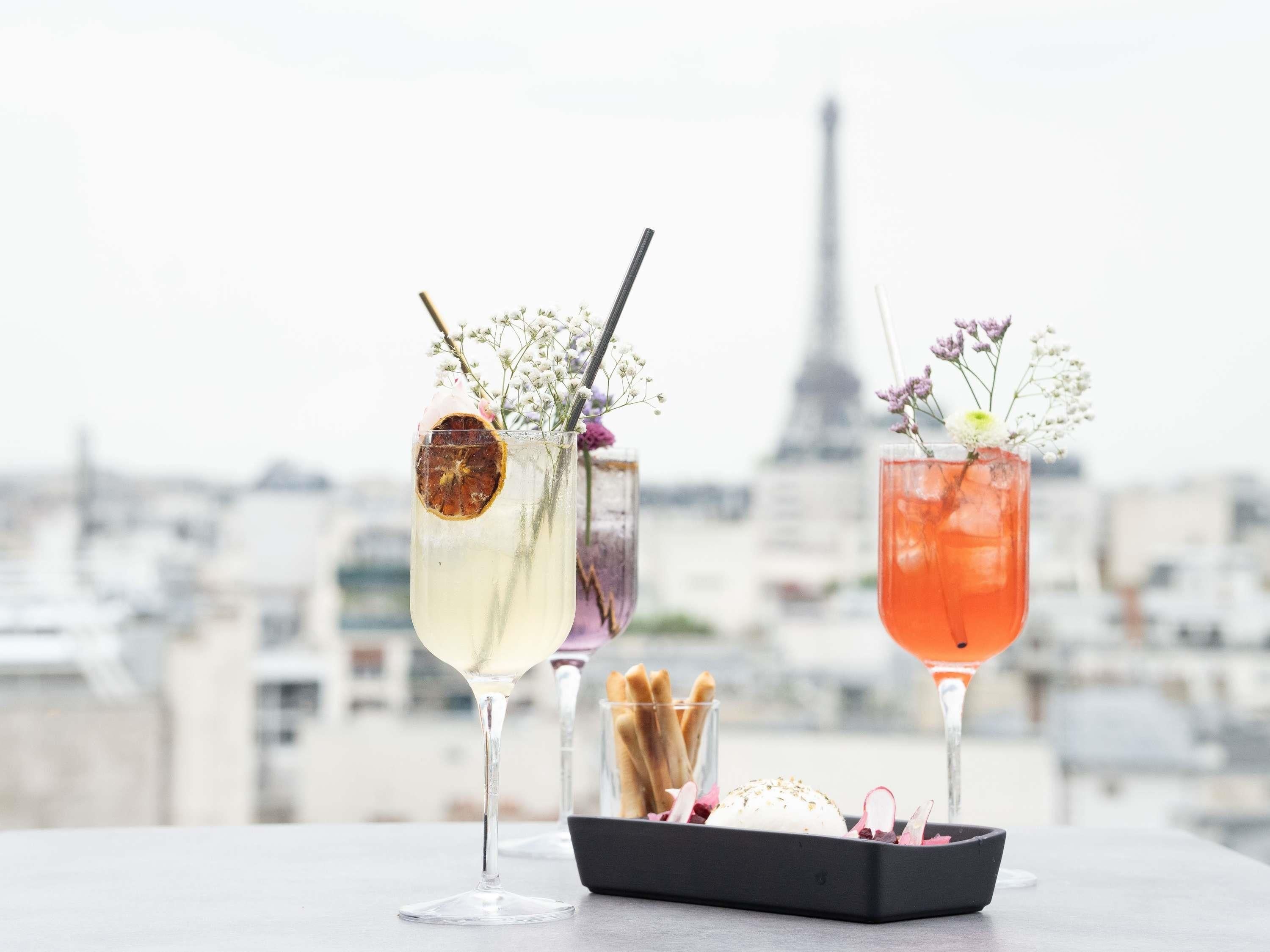Two cocktails with garnishes, a tray with crackers, and a cityscape with a tower in the background.