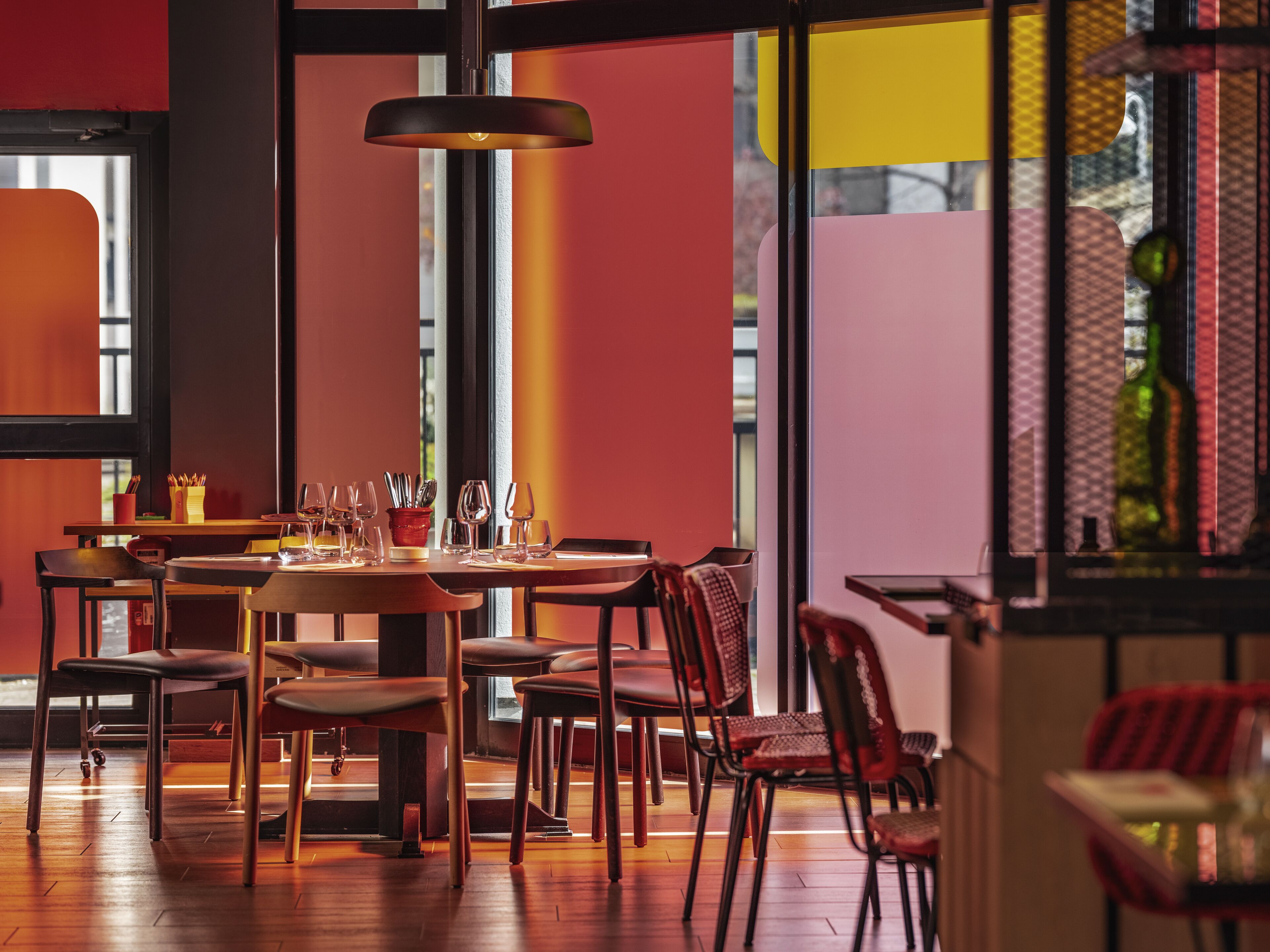 A restaurant interior with a wooden table set for dining, chairs, and a hanging light fixture.