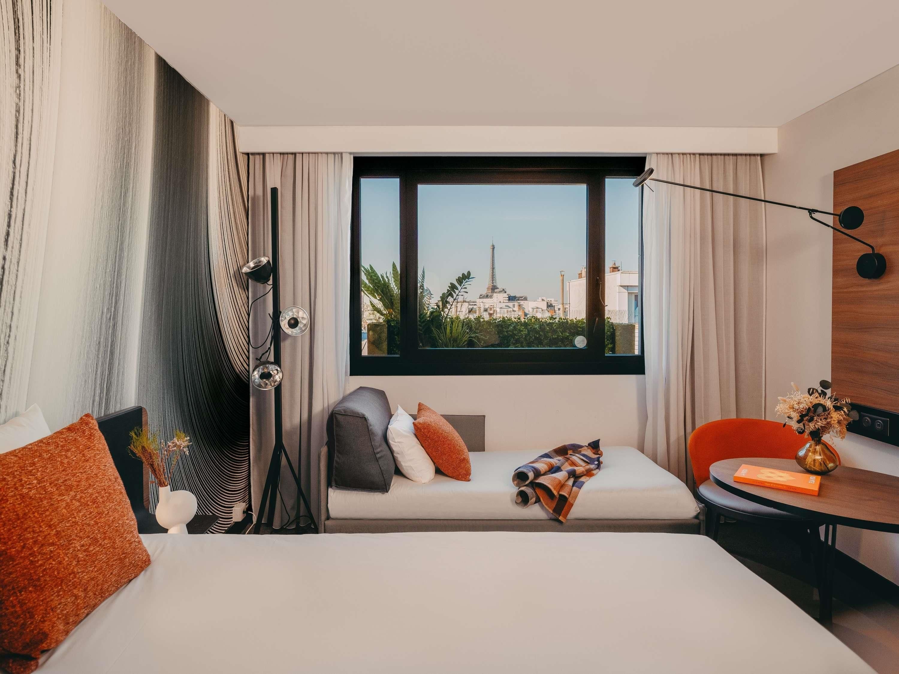 Een hotelkamer met een bed, een zithoek, een bureau en uitzicht op een stadsgezicht.