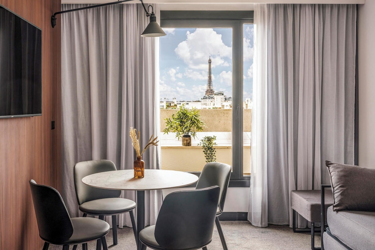 A modern room with a round table, two chairs, a sofa, and a view of the Eiffel Tower.