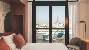Un dormitorio con una cama grande, una silla, un escritorio y vistas de la Torre Eiffel.