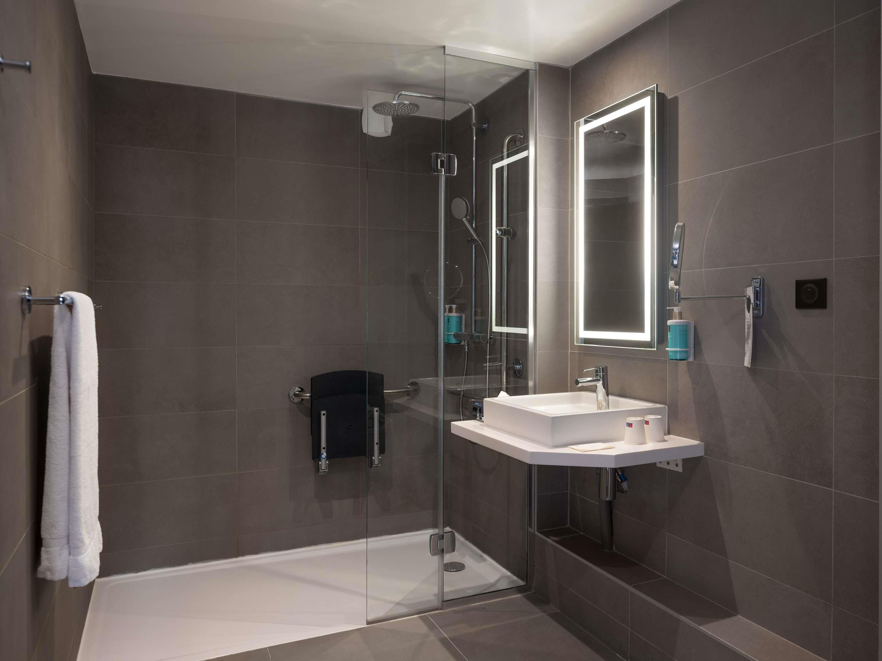 A modern bathroom with a glass-enclosed shower, a white sink, and a mirror with integrated lighting.