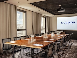 A conference room with a long table, chairs, and a projector screen displaying "NOVOTEL". - Novotel Paris Vaugirard Montparnasse (Paris)