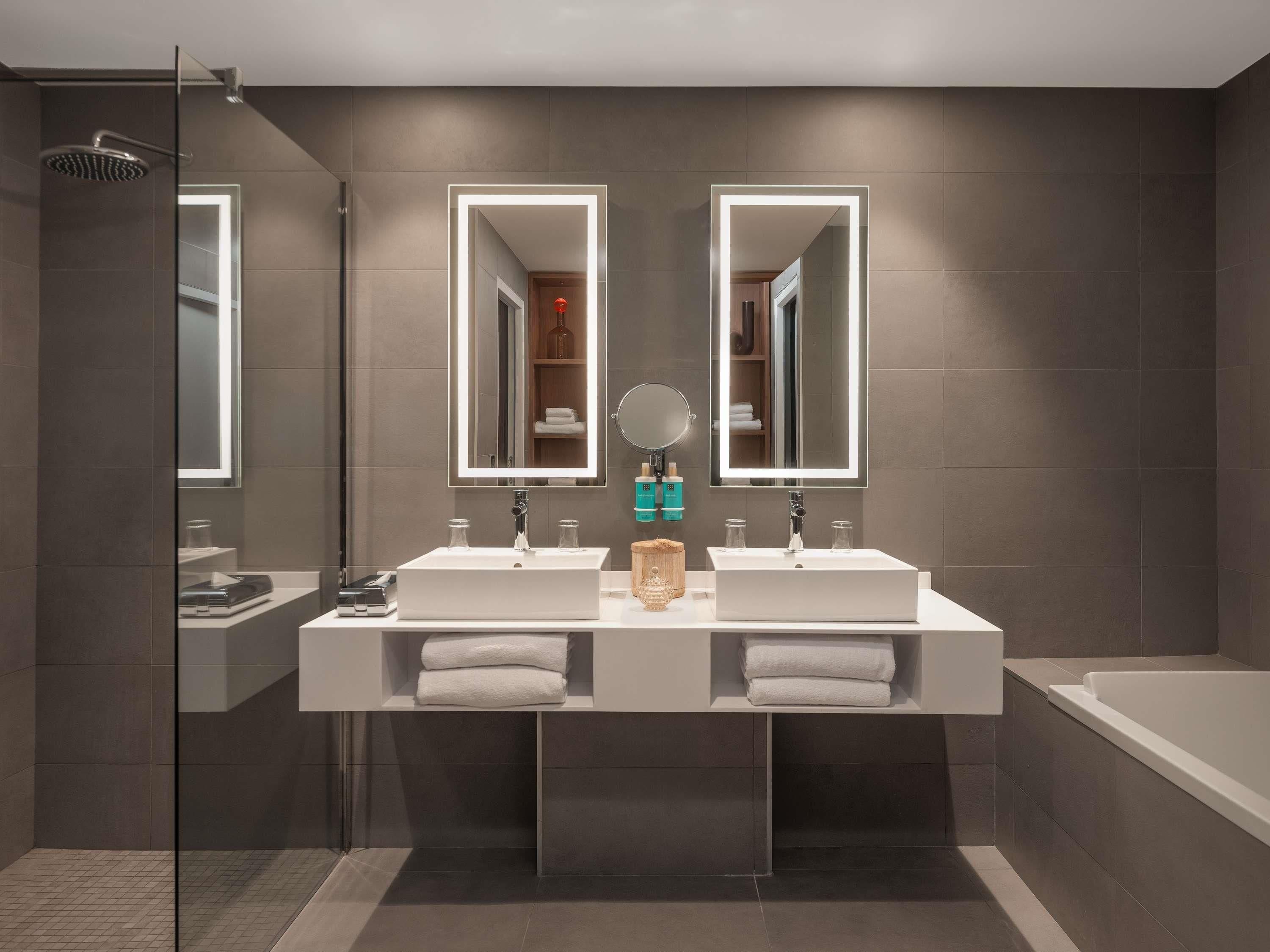 A modern bathroom with two sinks, a large mirror, and a shower.