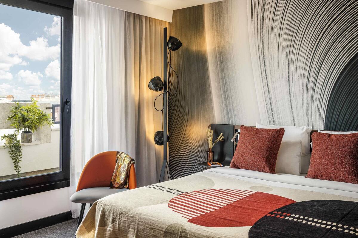 A modern hotel room with a large bed, a view of the city, and a balcony with plants.