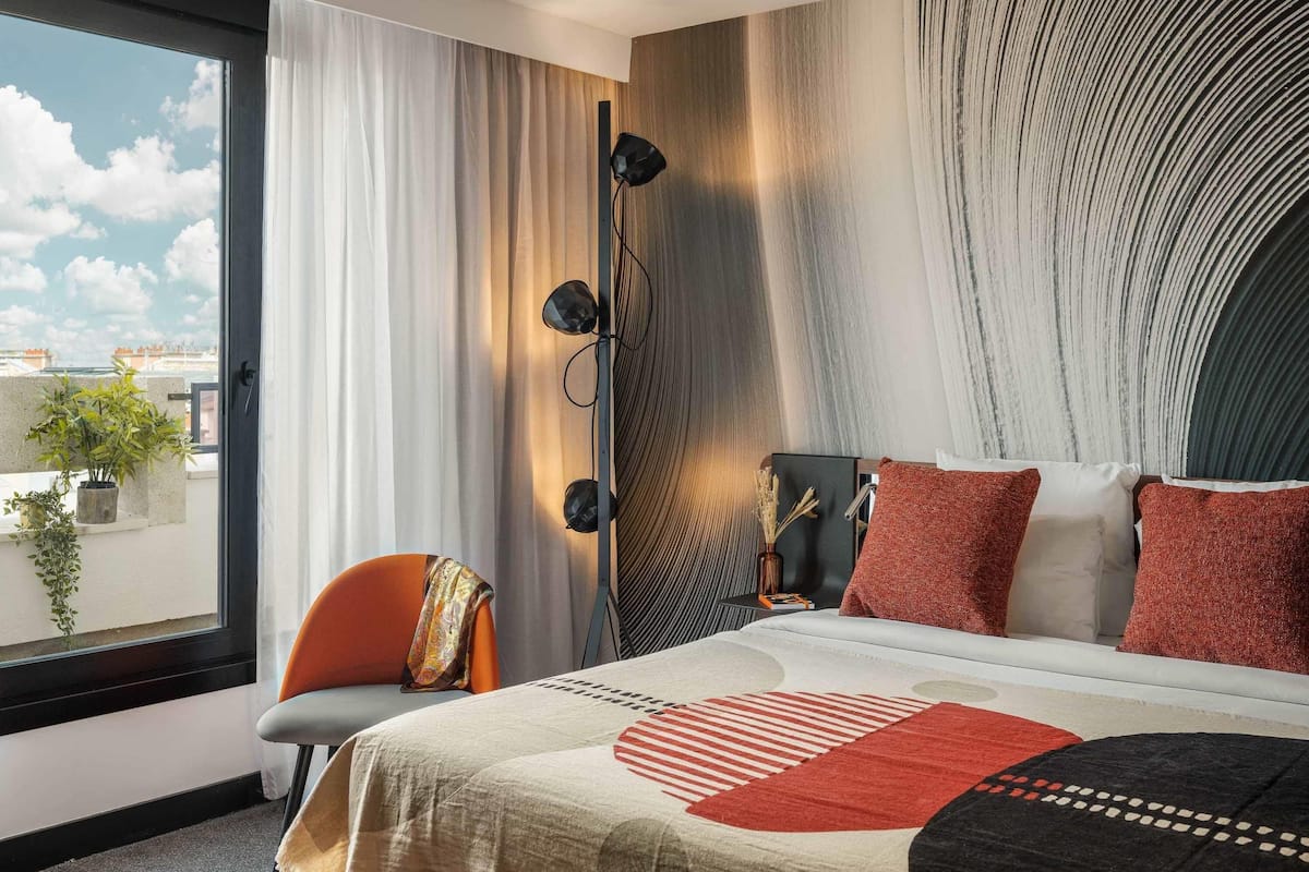 Une chambre dâhĂŽtel moderne avec un grand lit, une vue sur la ville et un balcon agrĂ©mentĂ© de plantes.