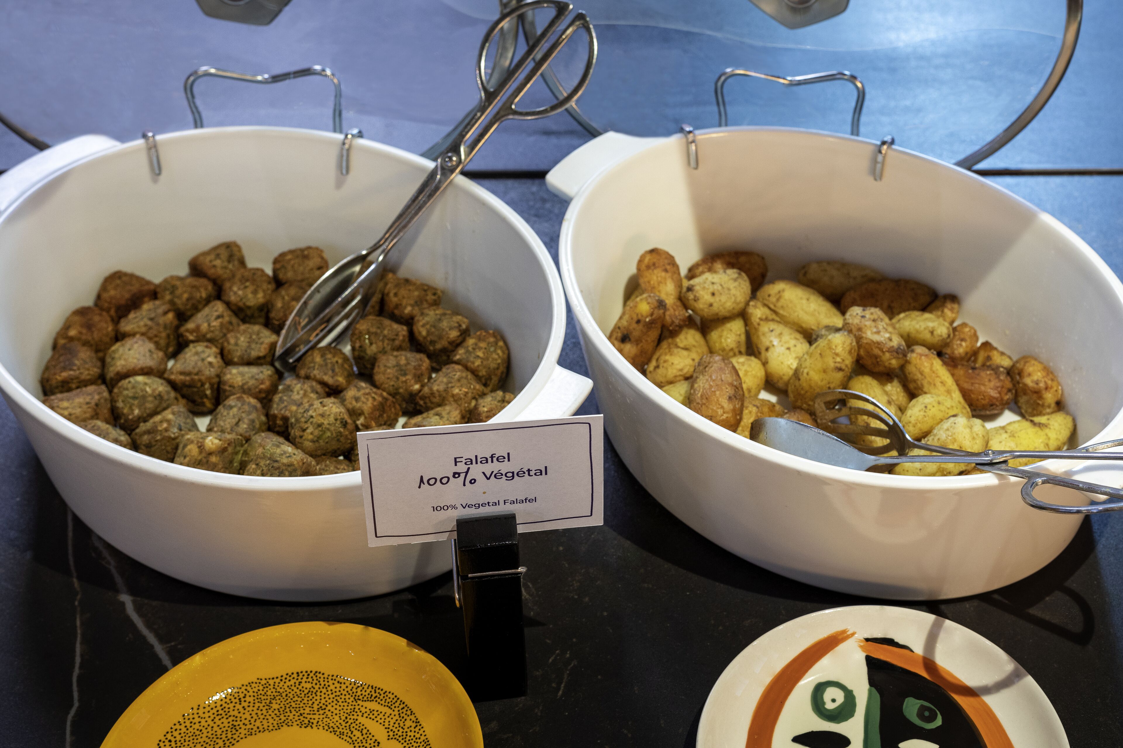 Dos porciones de falafel, una con la etiqueta '100% Falafel Vegetal', sobre una mesa con un letrero.