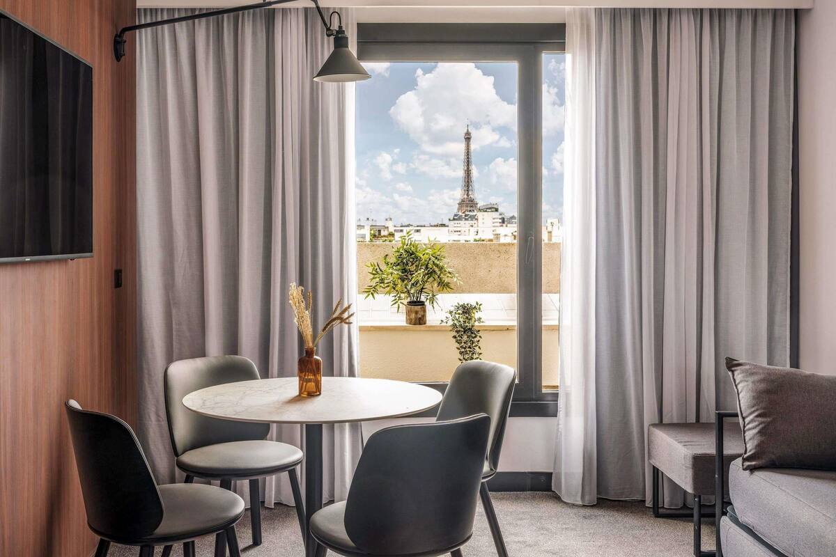 A modern room with a round table, chairs, a sofa, and a view of the Eiffel Tower.