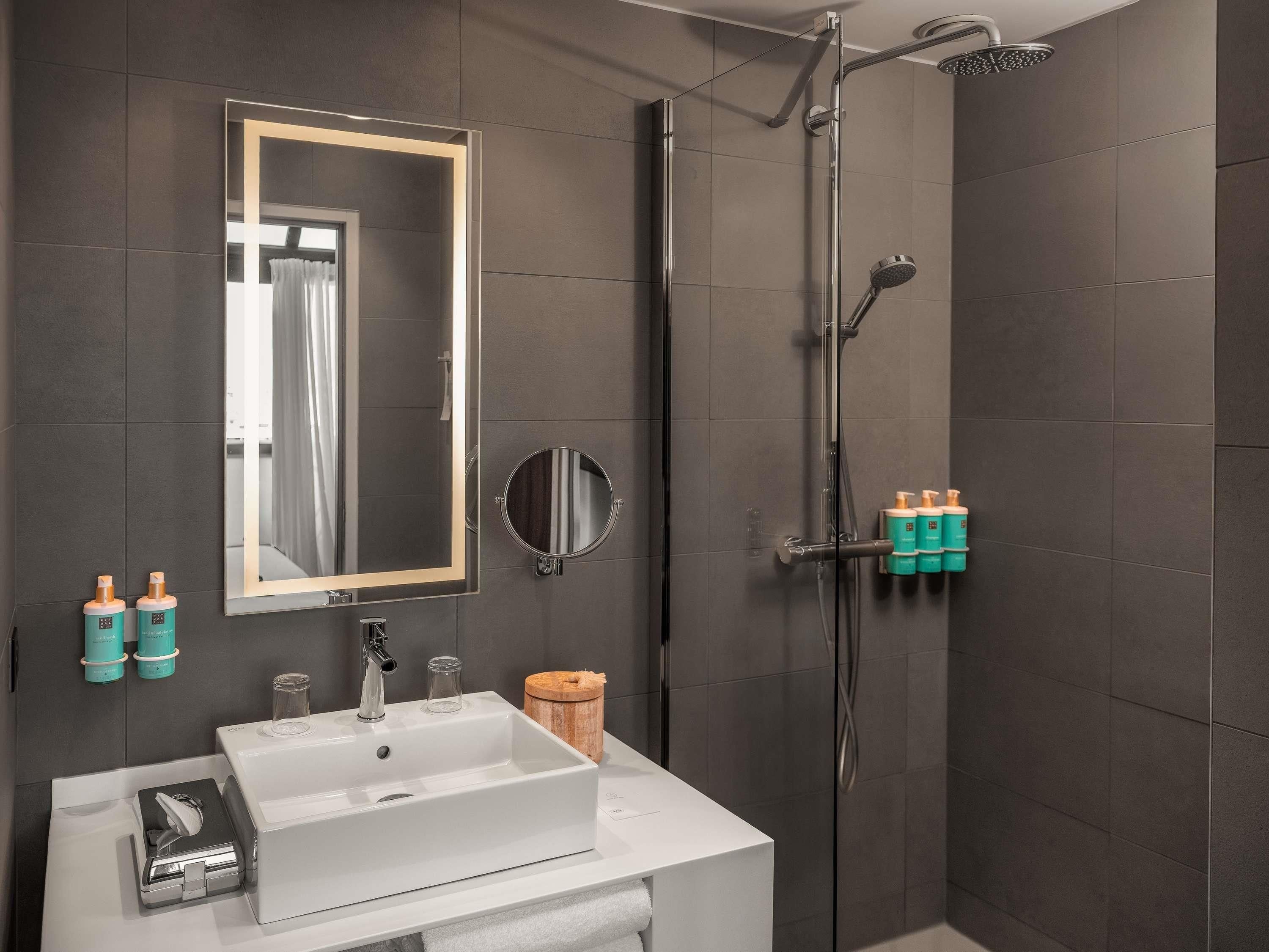 A modern bathroom with a large mirror, a sink, a shower, and toiletries.