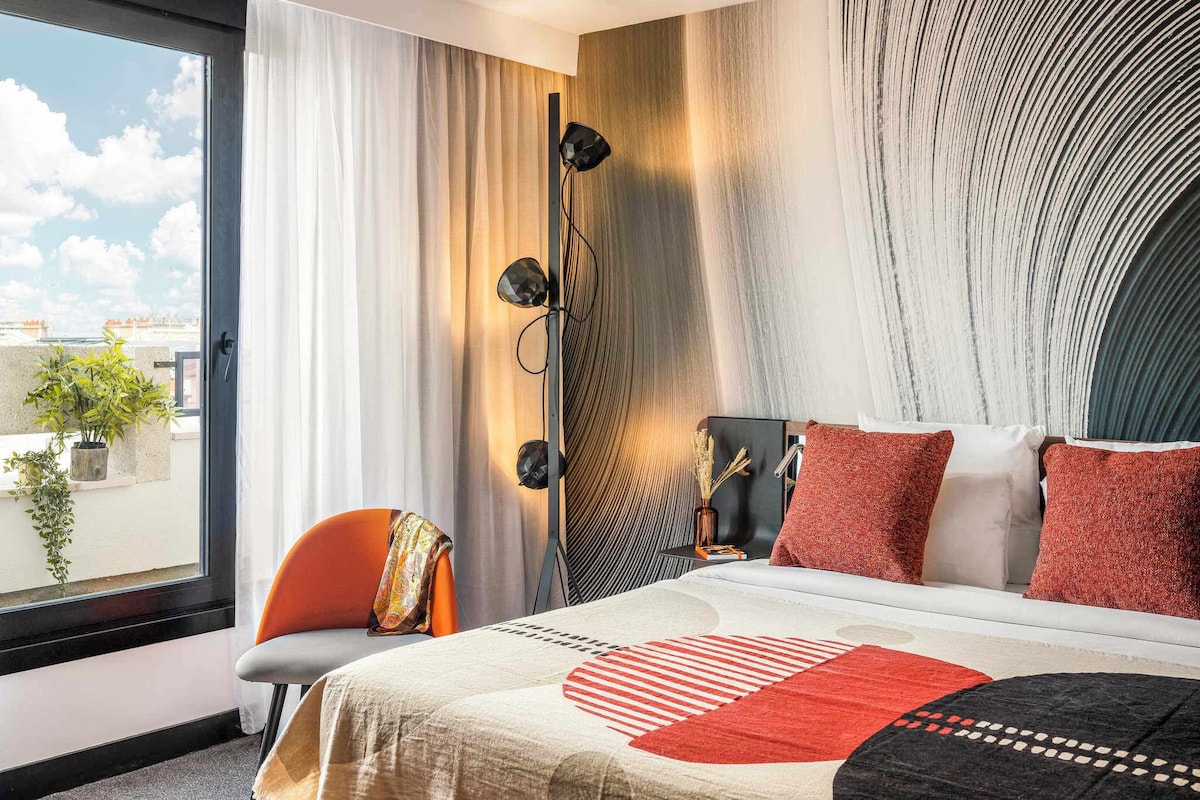 A modern hotel room with a large bed, a view of the city, and a large window with curtains.