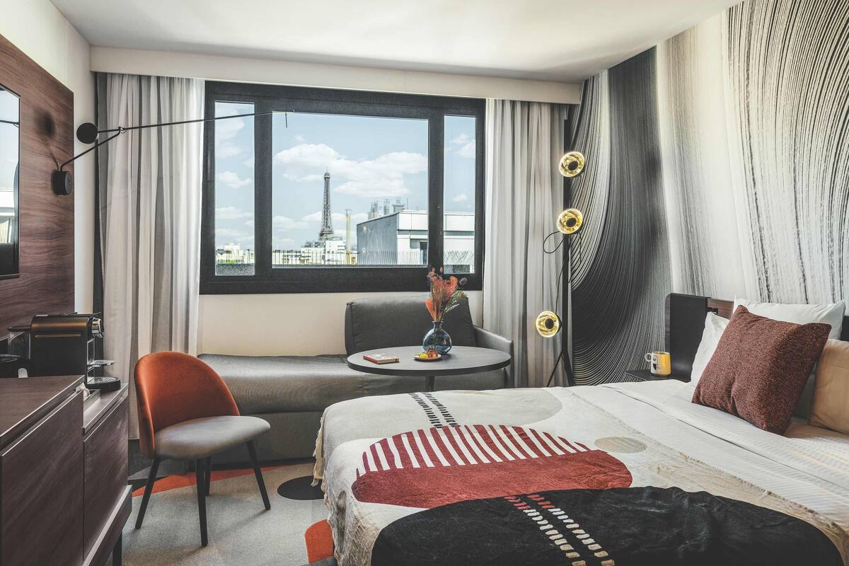A hotel room with a bed, a sofa, a desk, and a view of the Eiffel Tower.