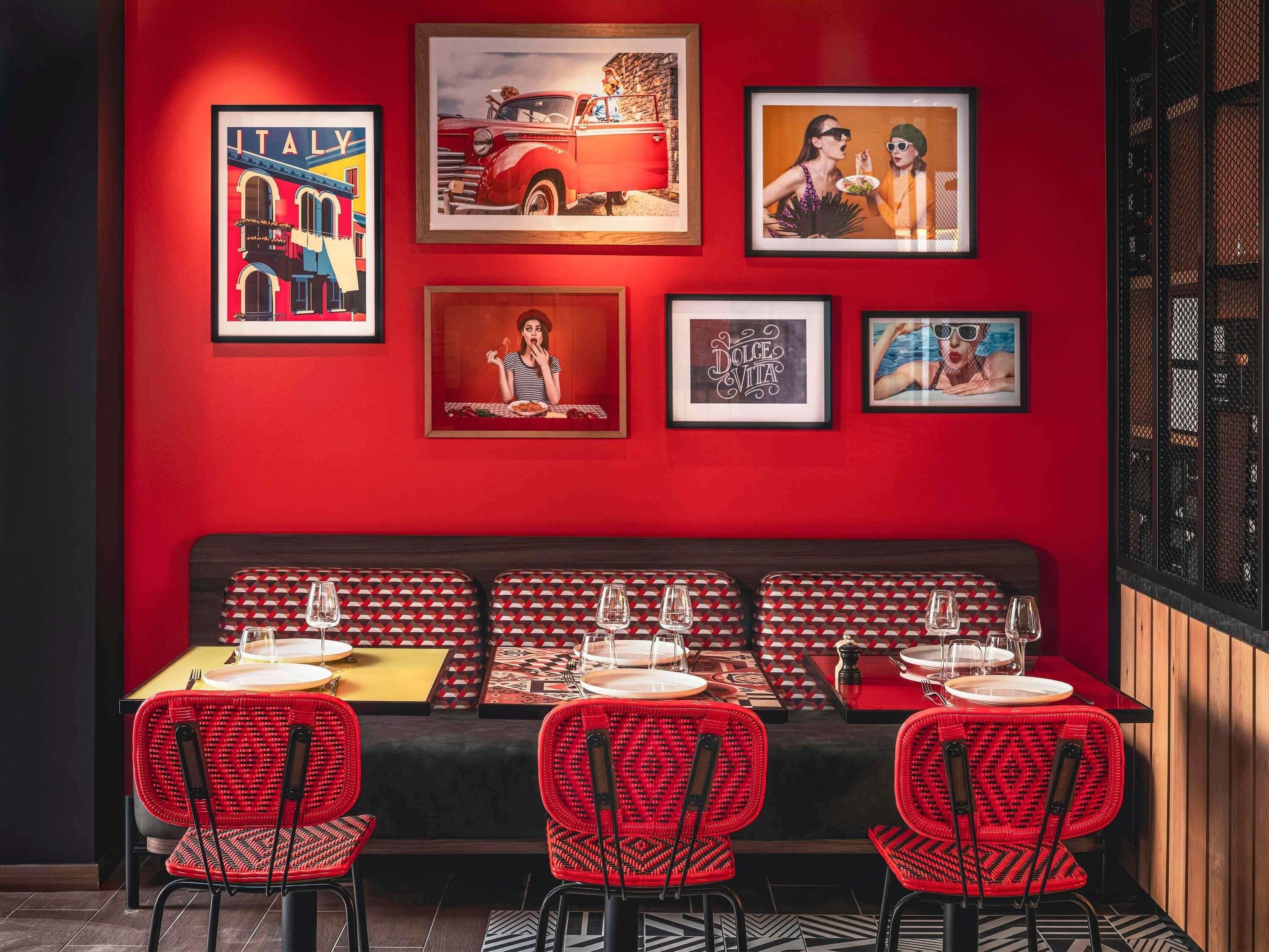 A red-themed restaurant with a black cushioned bench, red chairs, and framed pictures on the wall.