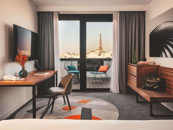 A hotel room with a desk, chair, bed, and a view of the Eiffel Tower.