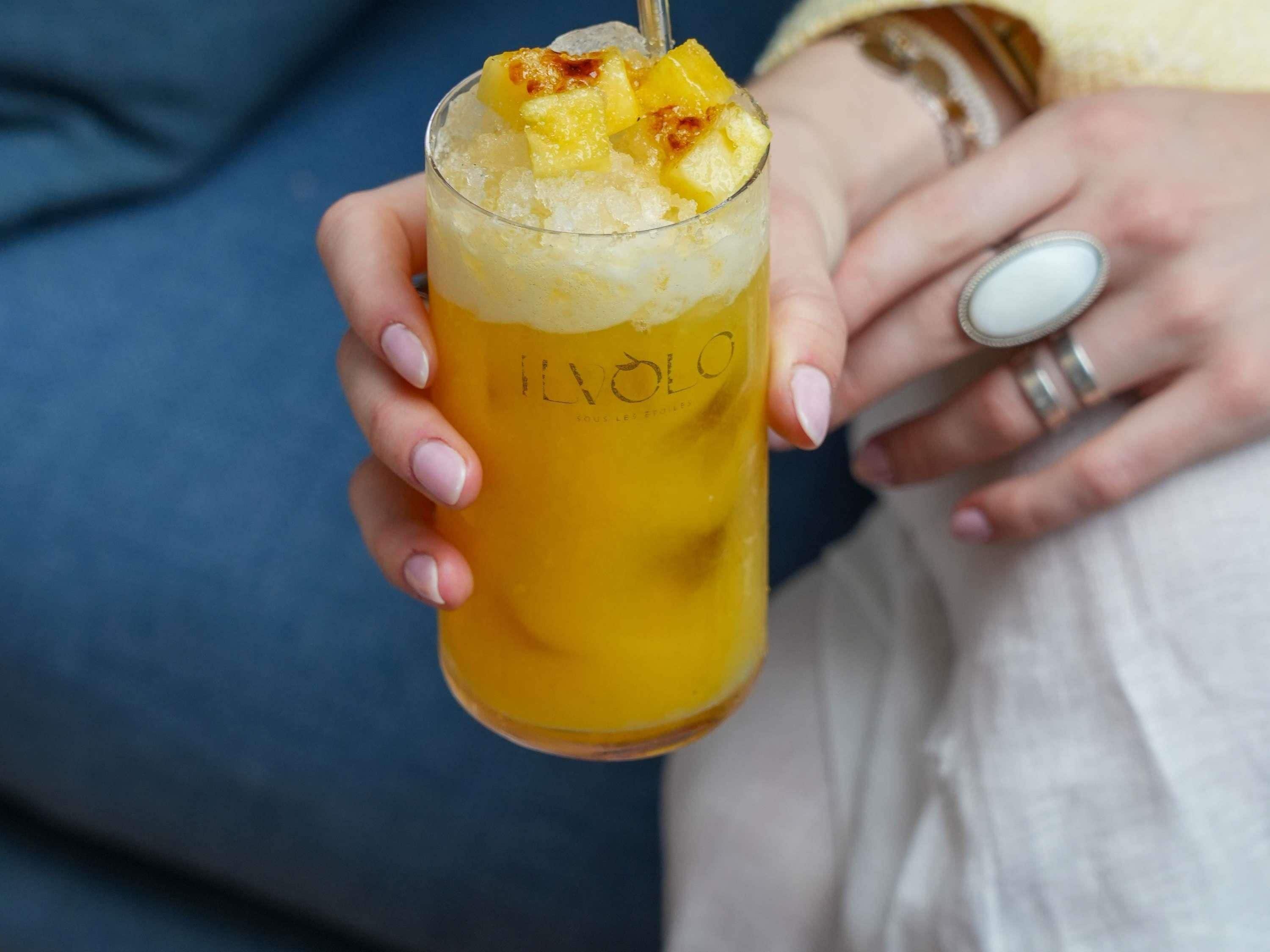 A person holding a glass with a yellow beverage and pineapple chunks.