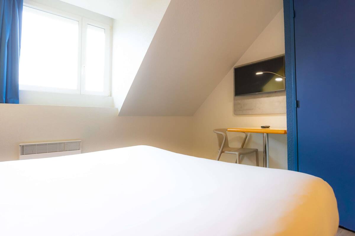 A room with a bed, a desk, a chair, a TV, and a window.