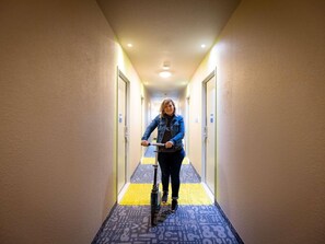 A person riding a scooter down a hotel hallway with patterned carpet and doors on either side. - ibis budget Besancon Centre Gare (Besancon)