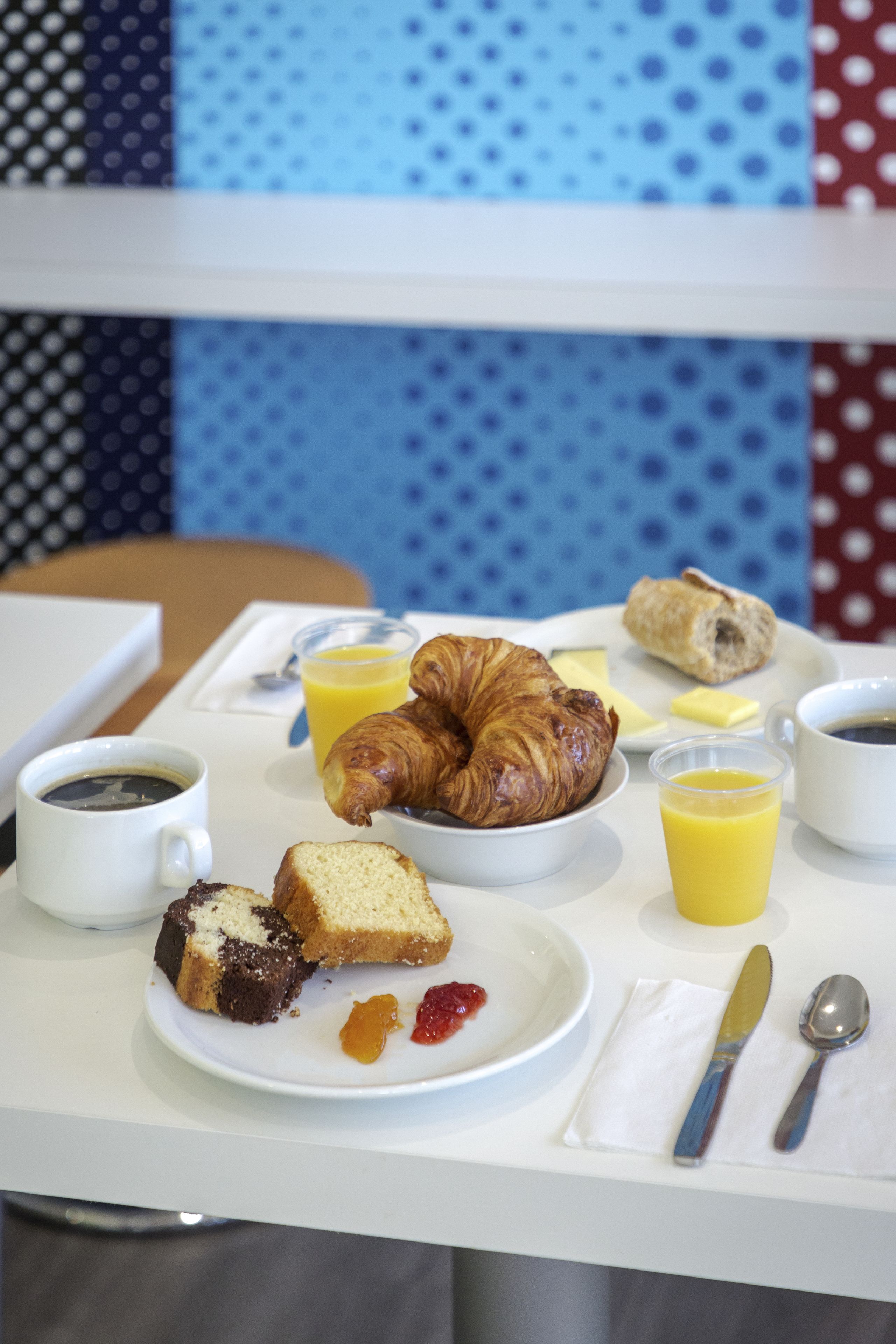 A breakfast table with croissants, pastries, coffee, juice, and a plate with cake and jam.