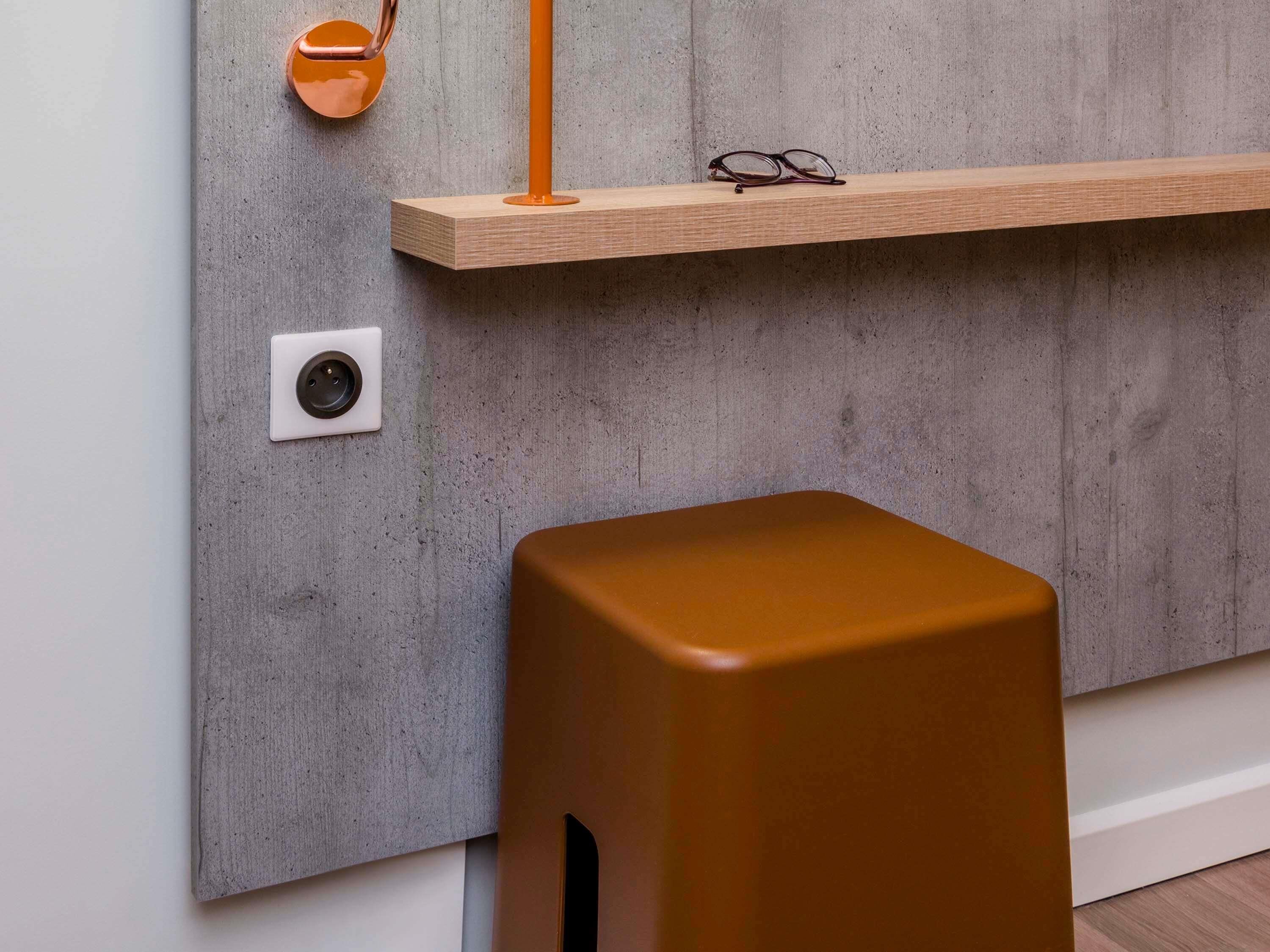 A modern interior with a concrete wall, a wooden shelf with glasses, and a brown stool.