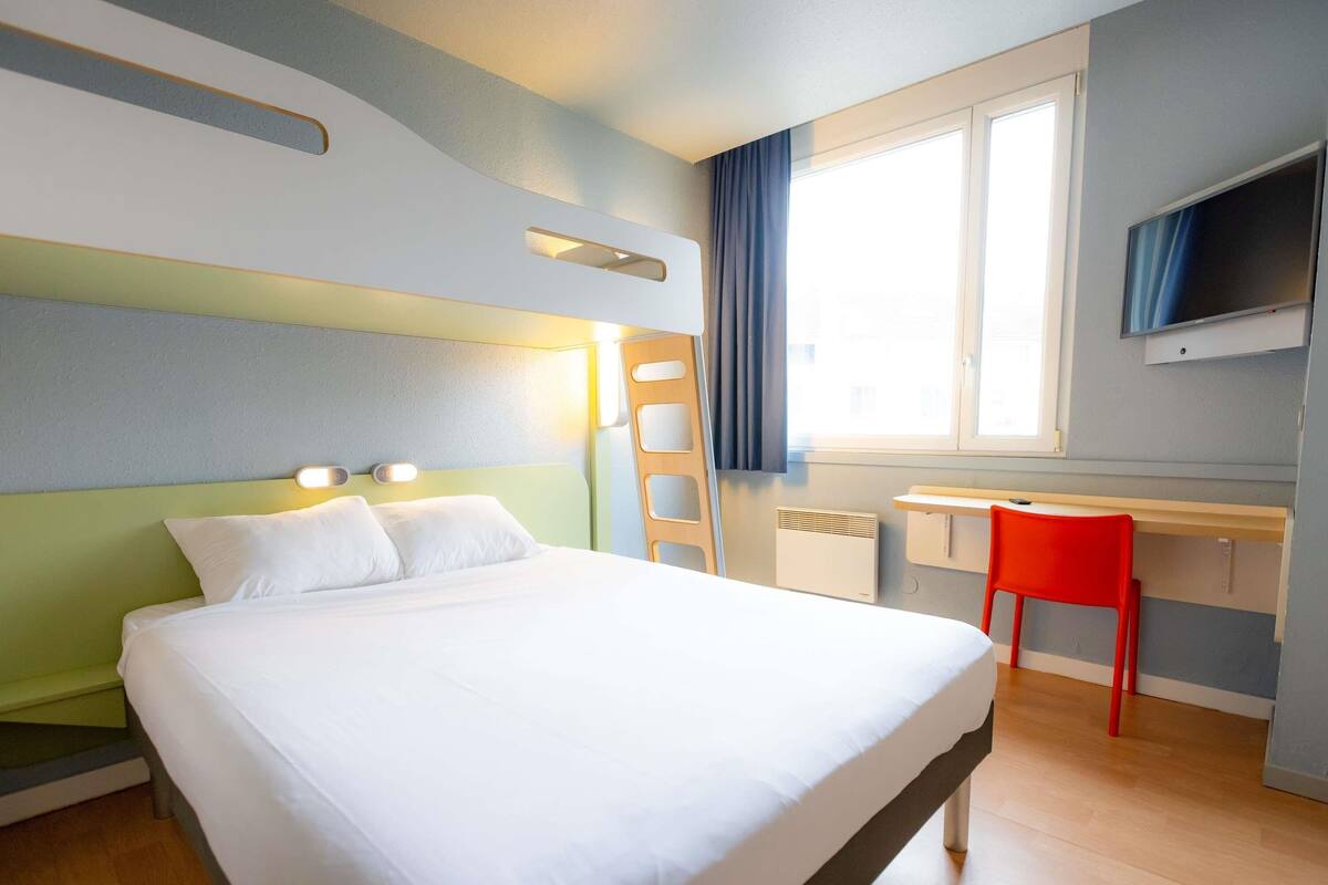 A hotel room with a bed, a desk, a chair, a TV, and a window.