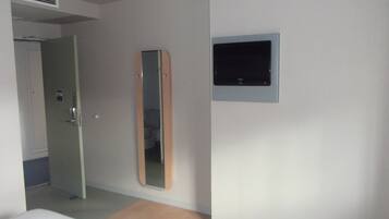 A bedroom with a bed, a door, a mirror, and a television mounted on the wall.