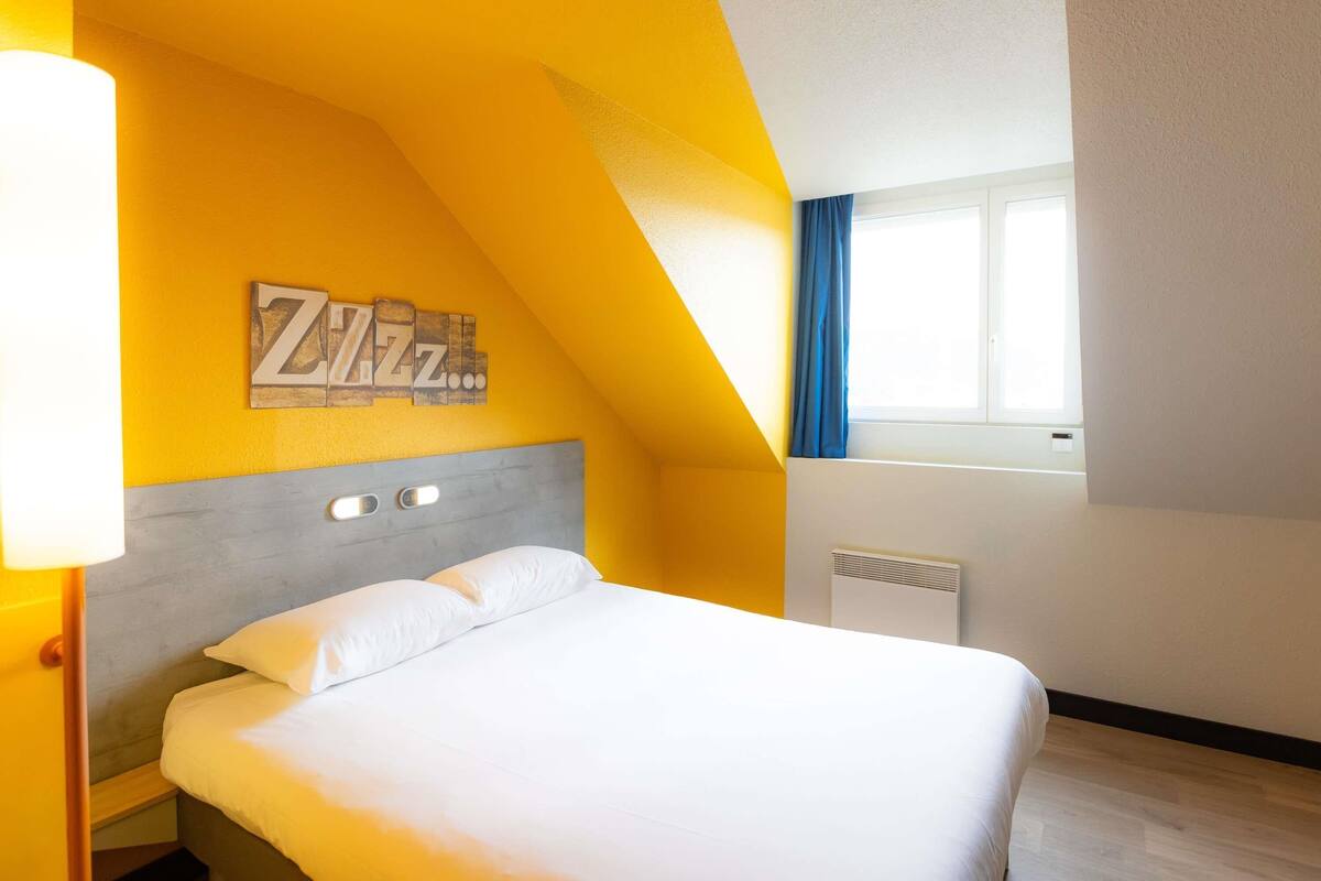 A bedroom with a bed, a wall-mounted artwork, a window with curtains, and a radiator.