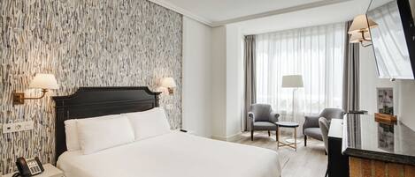 Quarto de hotel com uma cama grande, duas luminárias de cabeceira, uma escrivaninha com cadeira e um espelho amplo.