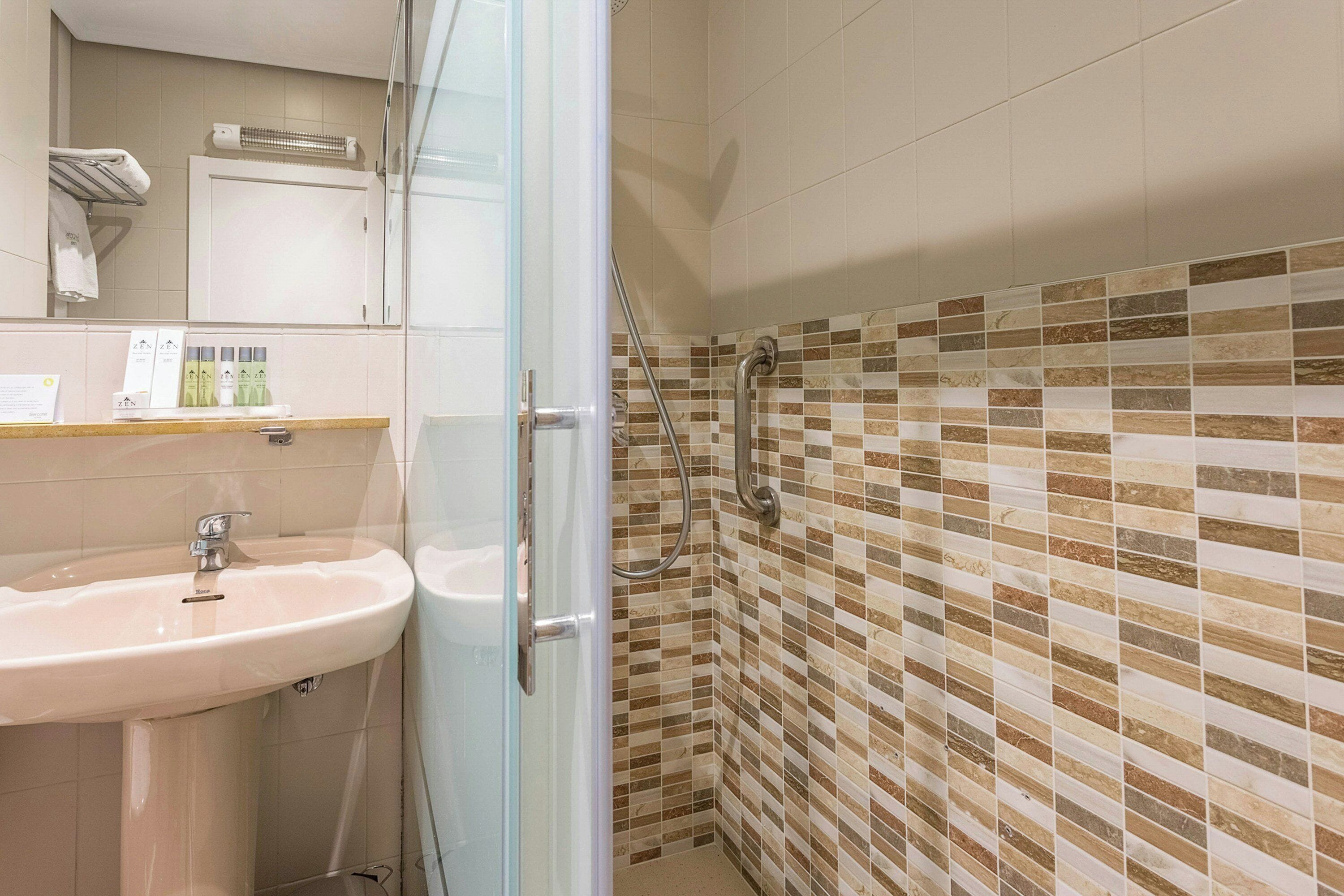 Un baño con cabina de ducha de vidrio, lavamanos y zona de ducha con azulejos.