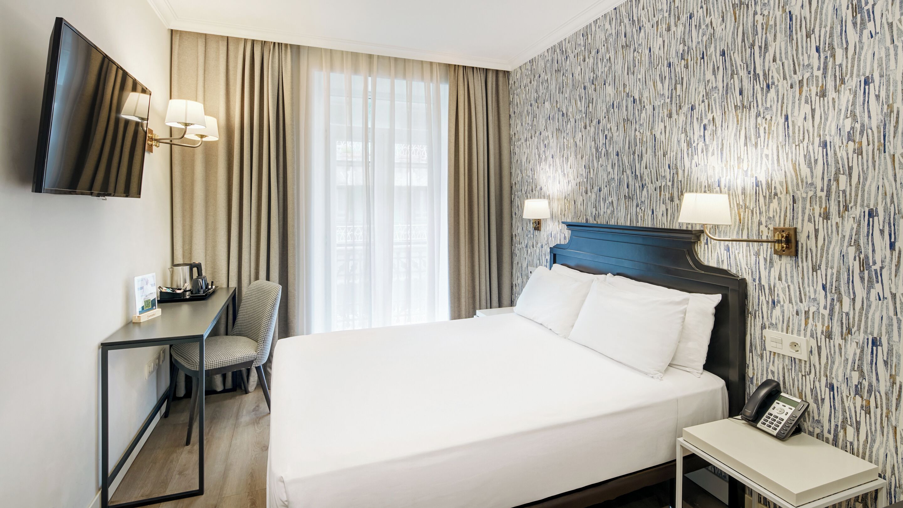 Een hotelkamer met een bed, een bureau met stoel, een televisie en een telefoon op een bijzettafeltje.