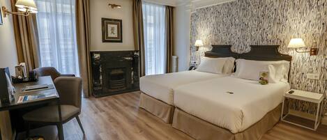 Una habitación de hotel con una cama grande, un escritorio con silla, una chimenea y un papel tapiz estampado.