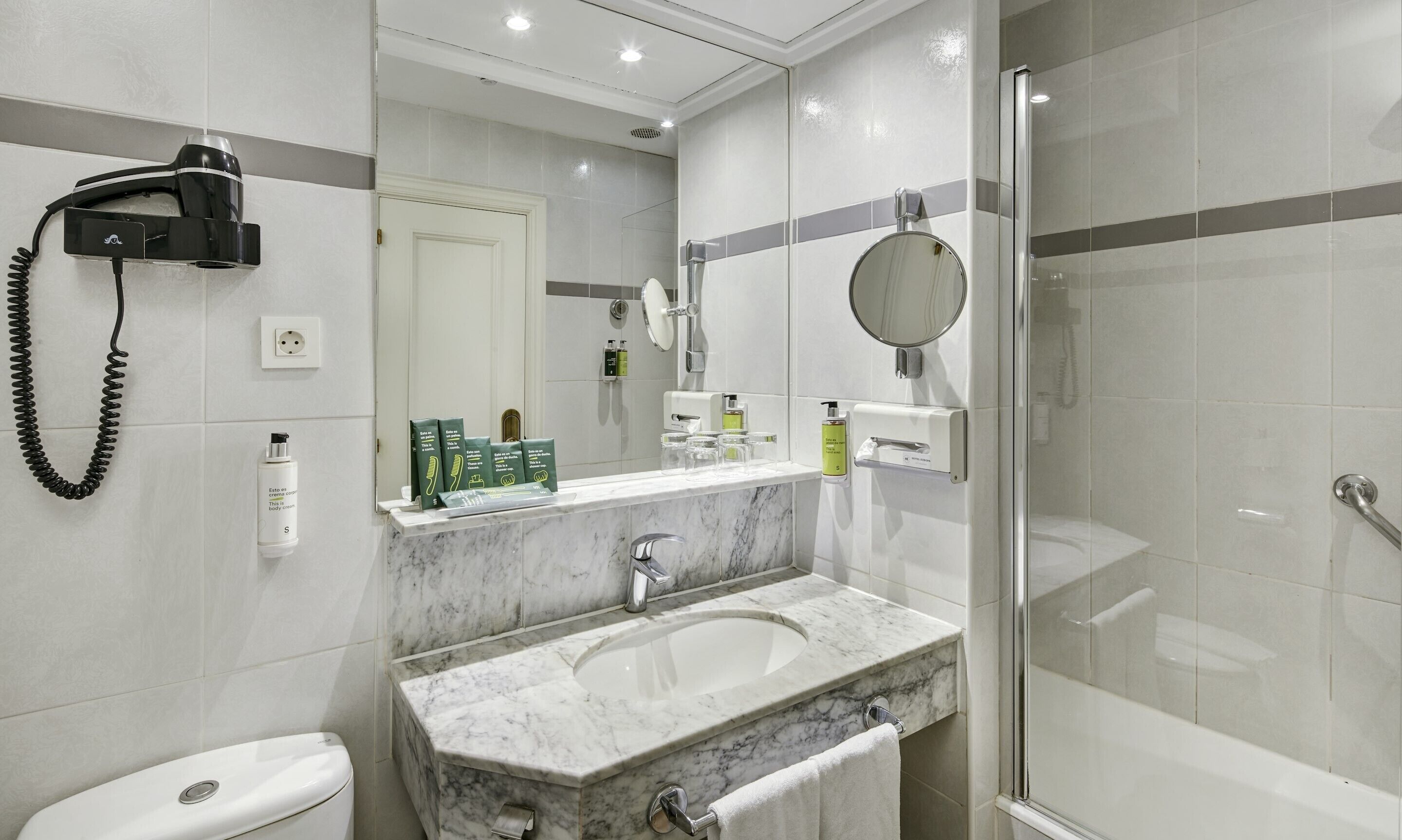 A modern bathroom with a marble sink, a handheld hair dryer, and a glass-enclosed shower.