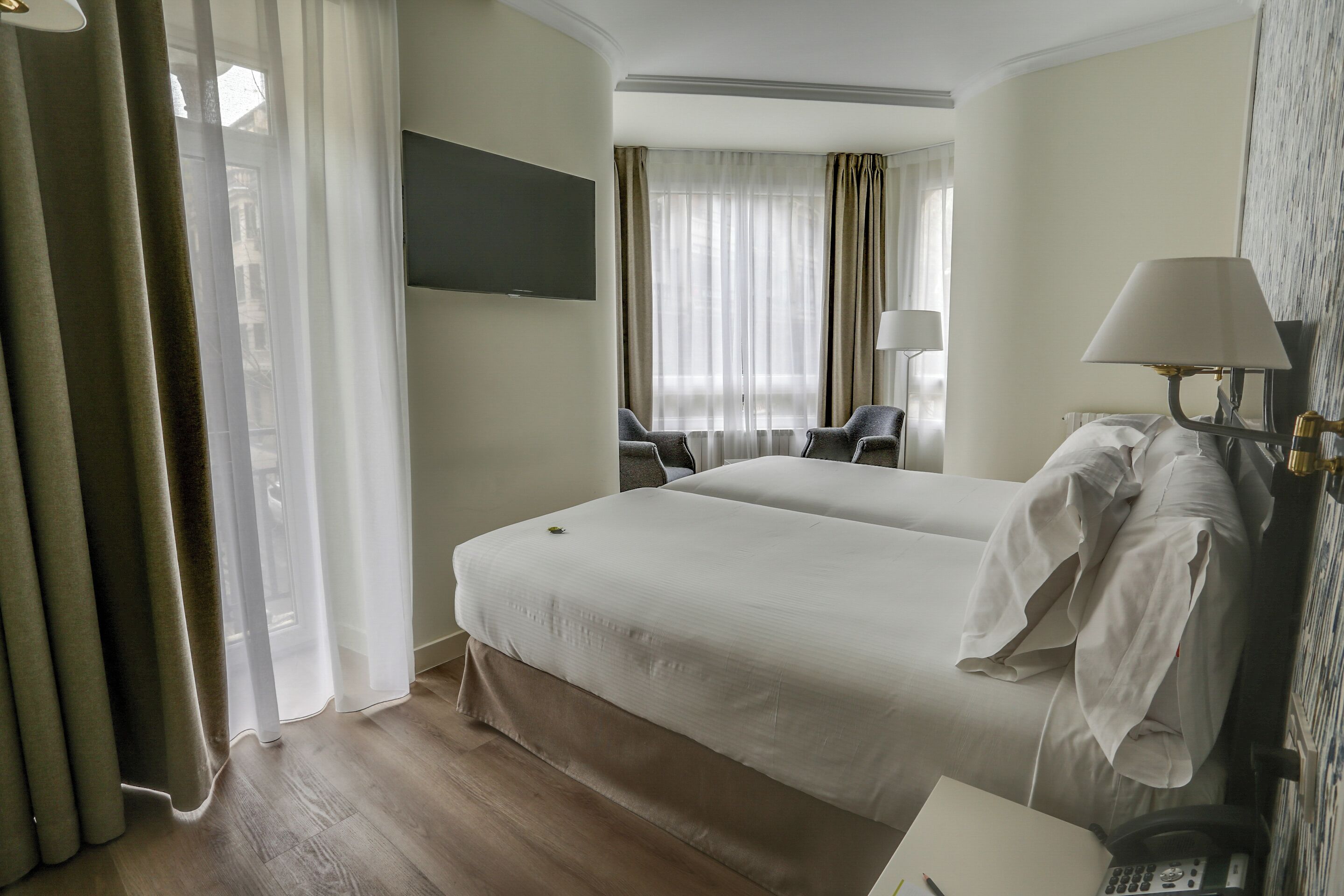 A hotel room with two beds, a desk with a telephone, and a TV mounted on the wall.