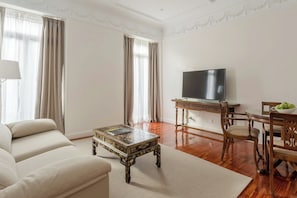 A living room with a sofa, a coffee table, a TV, and a dining area with chairs and a table. - Sercotel Hotel Europa (San Sebastián)