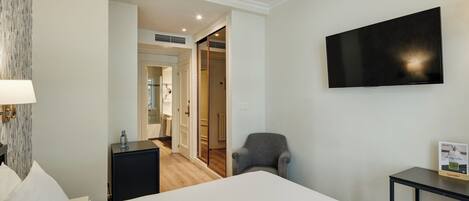 A hotel room with a bed, a desk, a chair, a TV, and a bathroom visible through an open door.