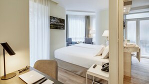 A hotel room with a large bed, a desk with a laptop, a chair, a bedside table with a lamp, and a view of the city through the window. - Sercotel Hotel Europa (San Sebastián)