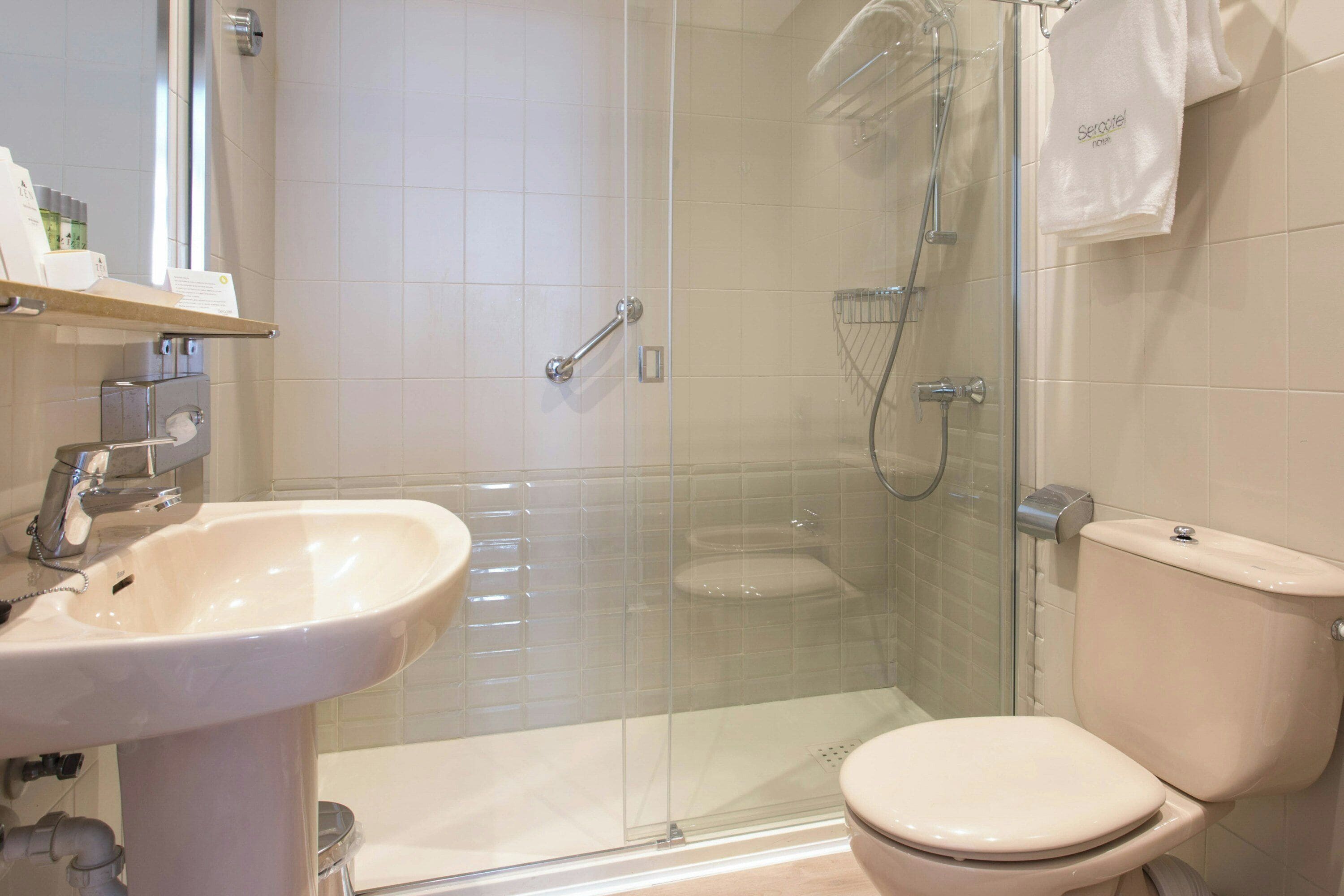 A bathroom with a glass-enclosed shower, a white sink, and a toilet.