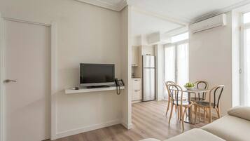 Una sala de estar moderna con un televisor de pantalla plana, un comedor con mesa y sillas, y una cocina con refrigerador.