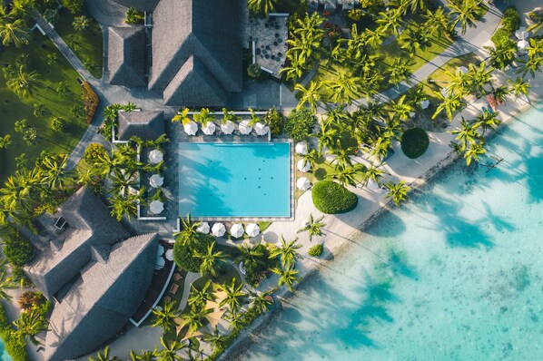 An aerial view of a resort with a swimming pool surrounded by palm trees and a beach.