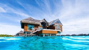 Een ruime, meerlaags bungalow boven water met rieten dak, gebouwd op palen boven helder turquoise water.