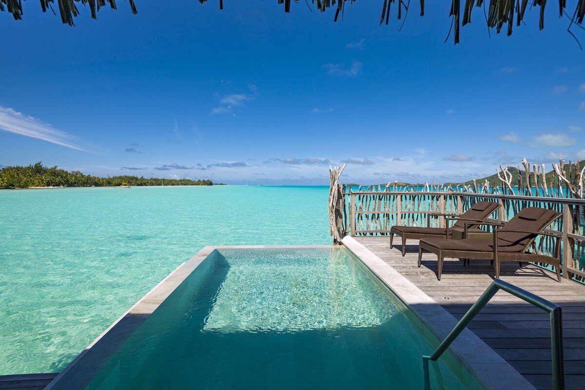 An infinity pool with a wooden deck, lounge chairs, and a view of the ocean.