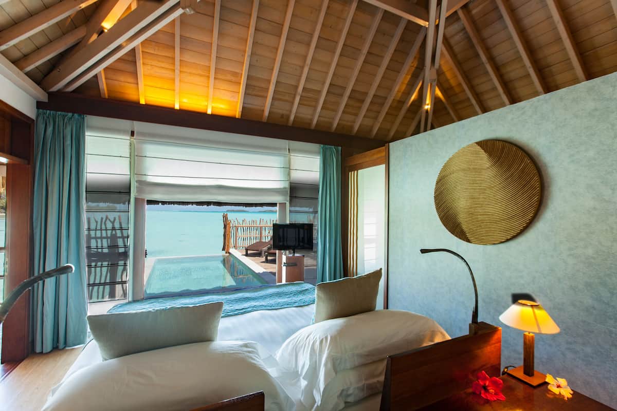 Een hotelkamer met een bed, een bureau, een lamp en uitzicht op zee.
