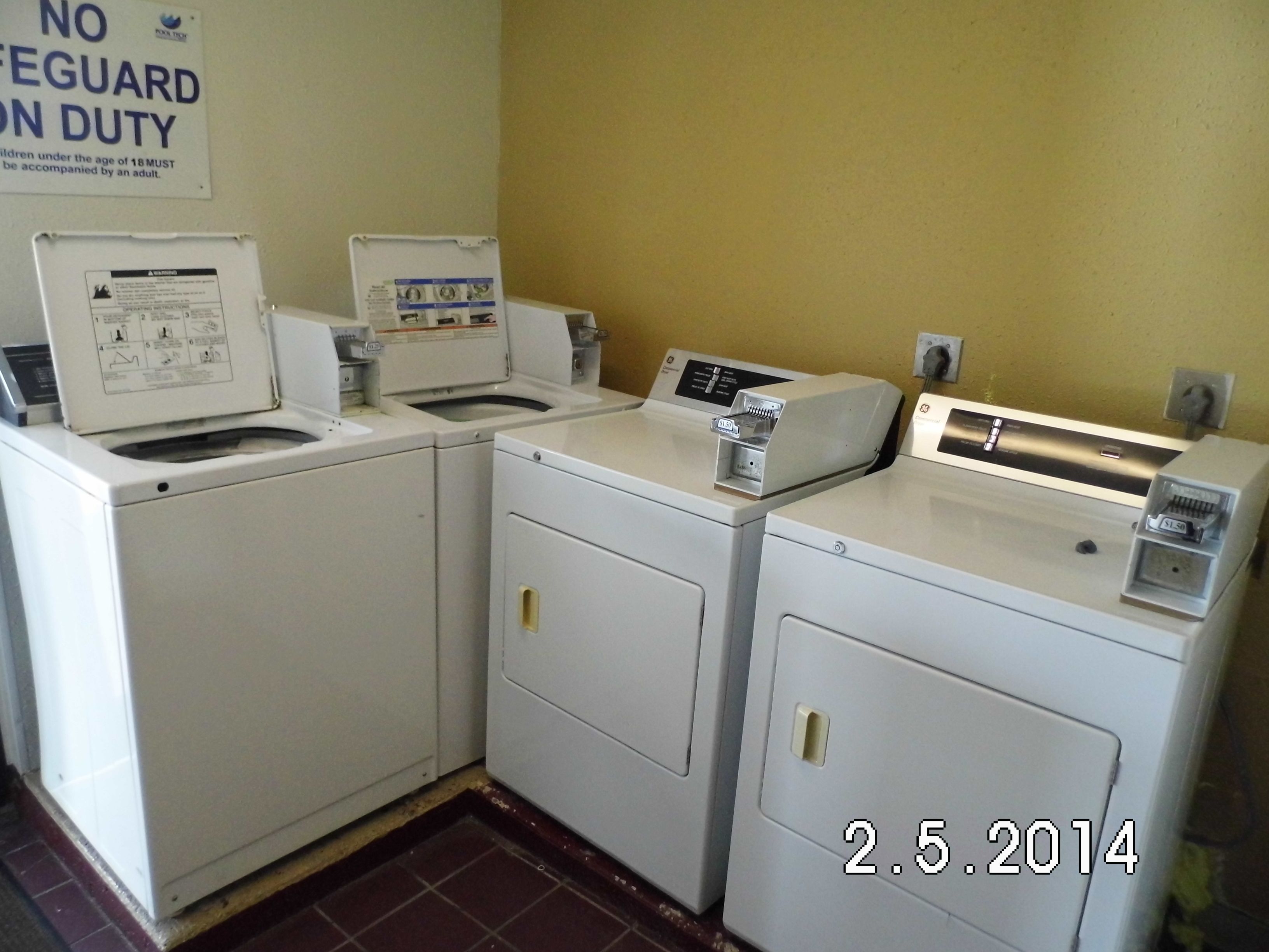 A laundry area with two washing machines and a dryer. A sign above the machines states "NO LIFEGUARD ON DUTY."