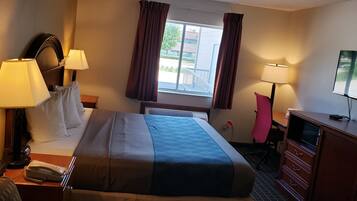 A hotel room with a bed, two bedside lamps, a TV, a desk with a telephone, and a dresser.