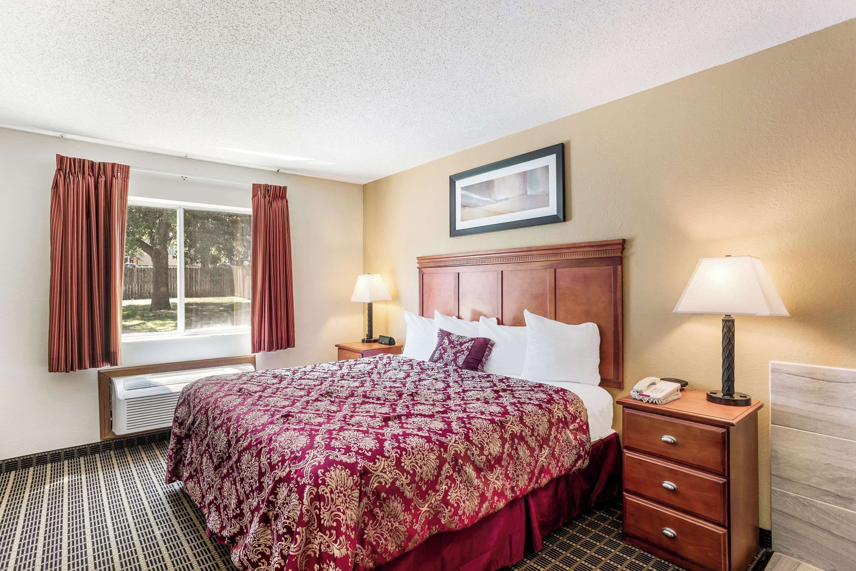 A hotel room with a large bed, two bedside tables with lamps, a framed picture on the wall, and a window with curtains.