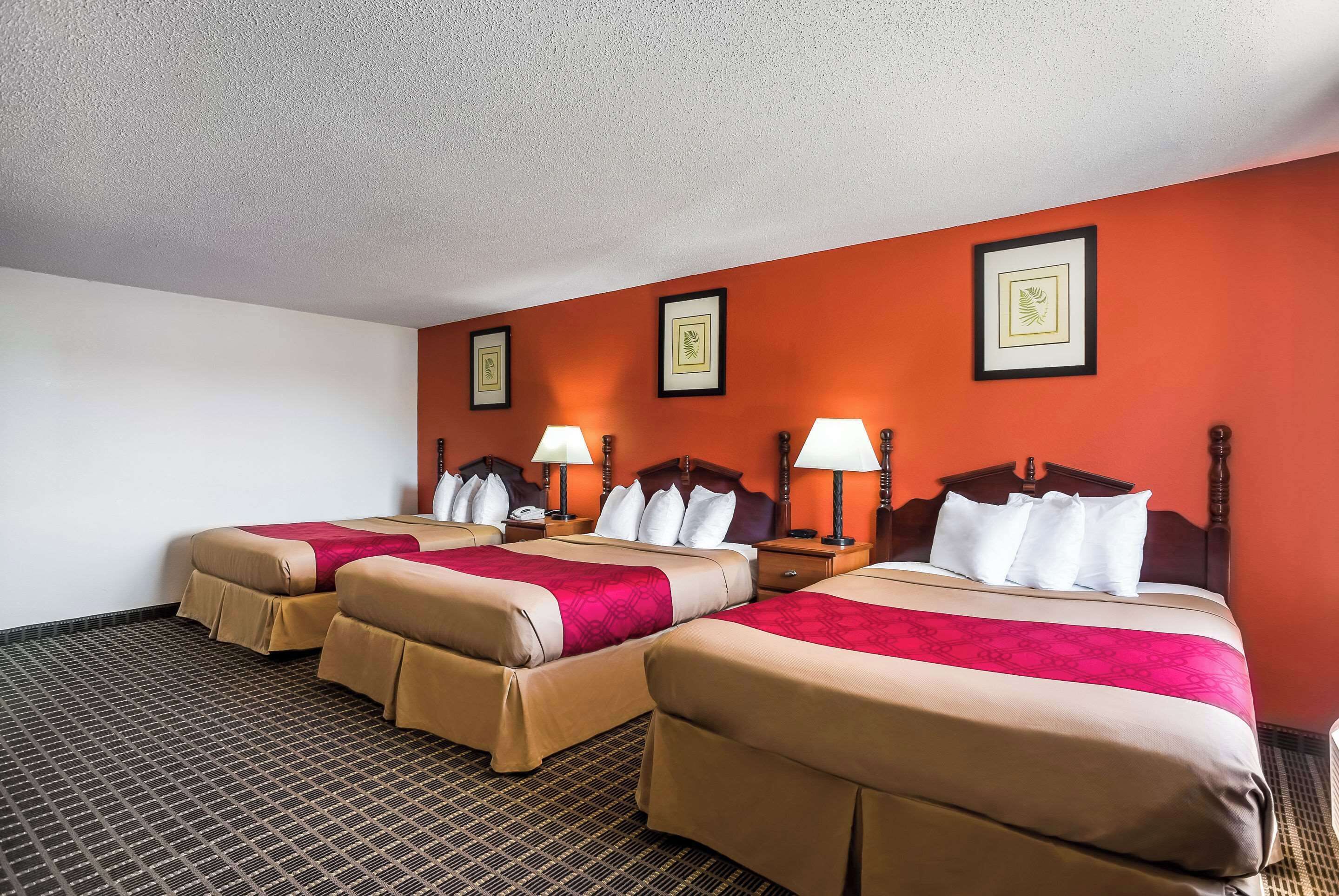 Habitación de hotel con tres camas, cada una con cabecera y lámparas de noche.