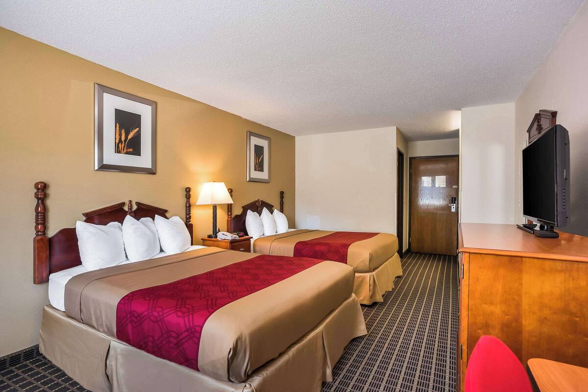 A hotel room with two beds, a desk, a television, and a door leading to another room.