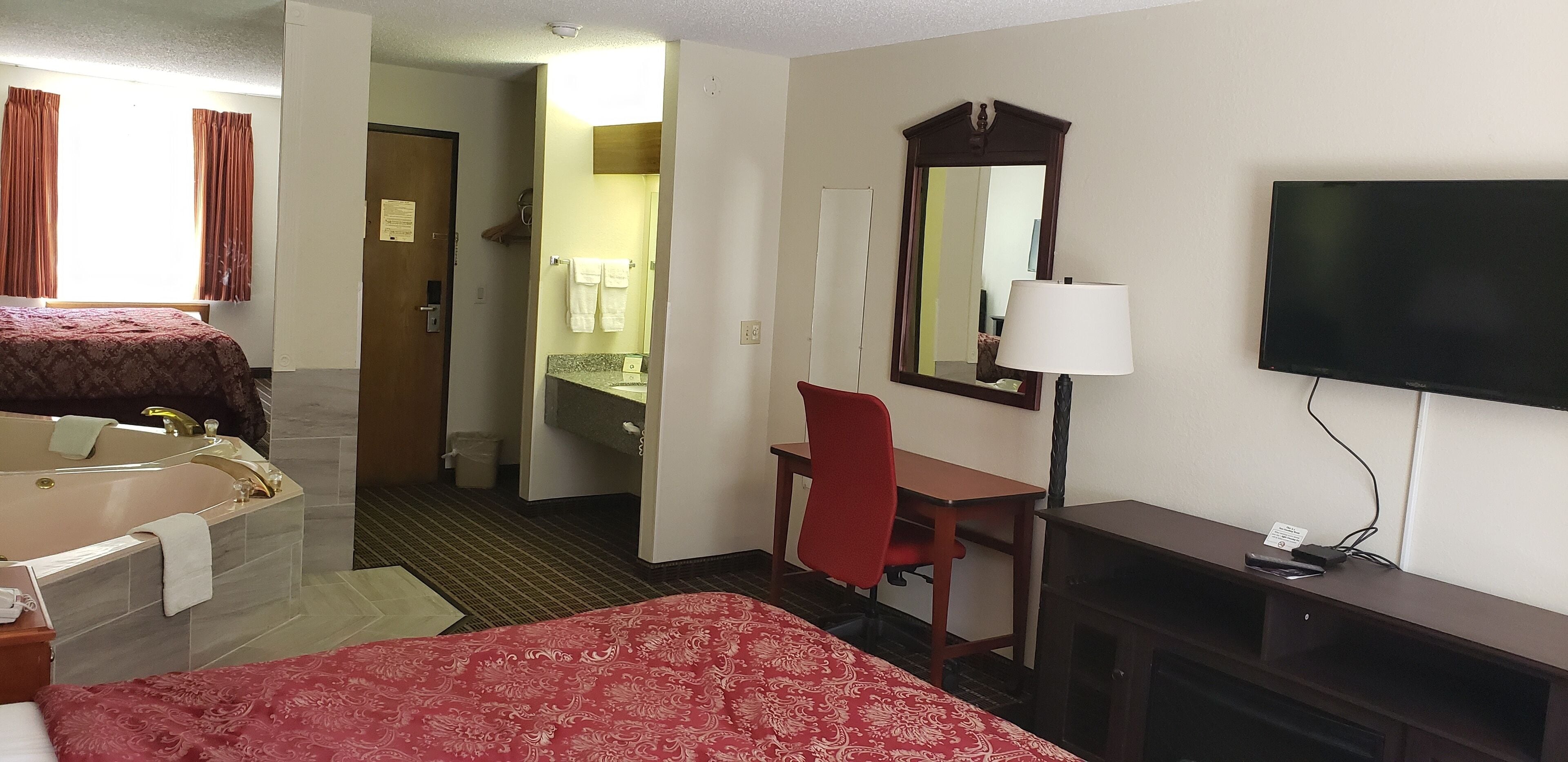 Ein Hotelzimmer mit Bett, Schreibtisch, Stuhl, Fernseher und einem Badezimmer mit Spiegel sowie einem Fenster mit Vorhängen.