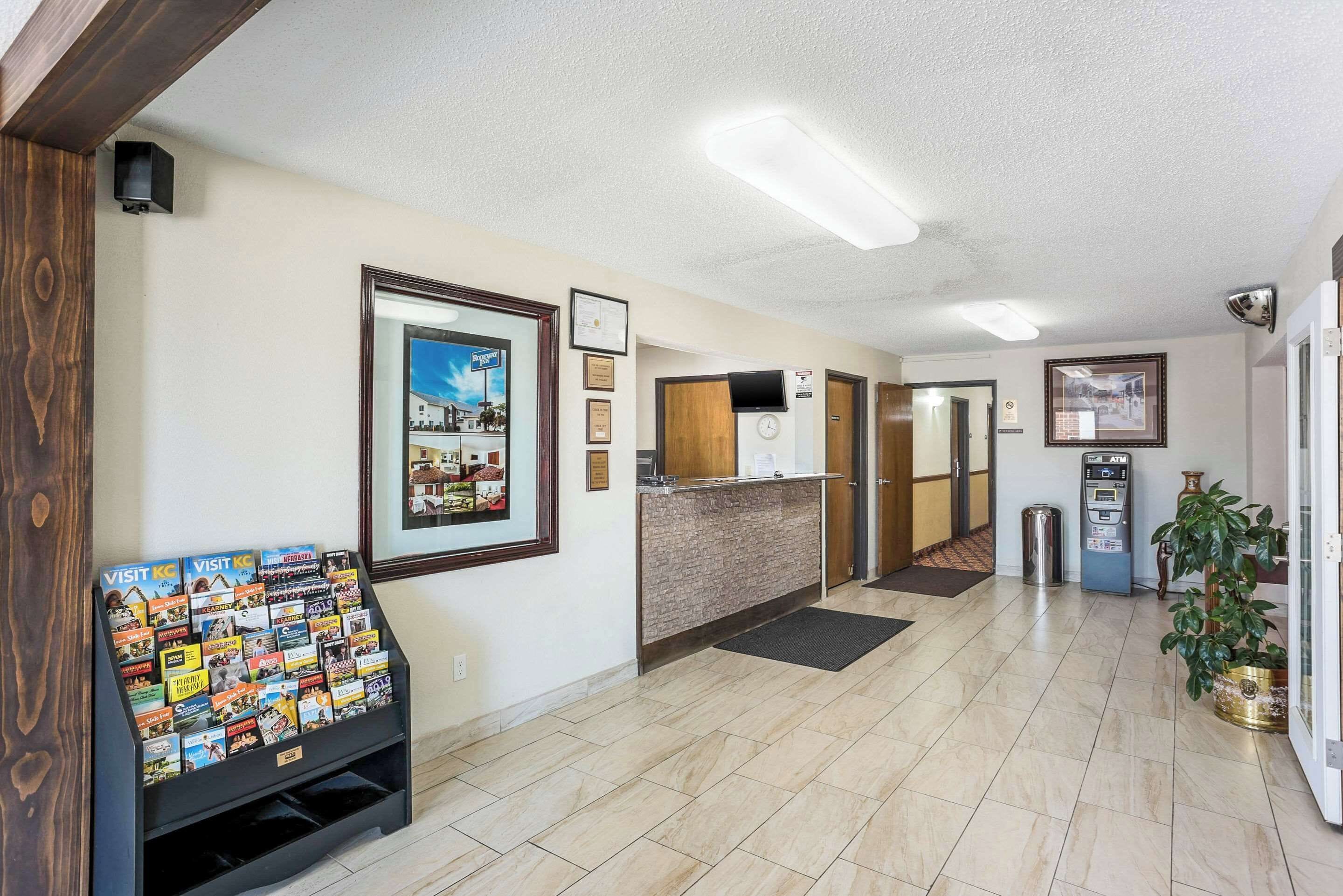 A hotel lobby with a reception desk, framed pictures on the wall, a display of brochures, and an ATM machine.