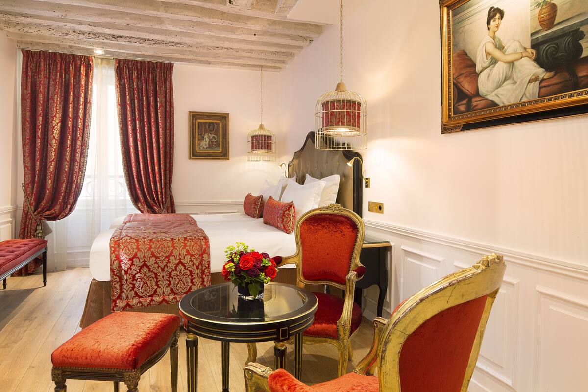 Une chambre d’hôtel avec un lit, un coin salon comprenant une table et des chaises, un vase de fleurs et un tableau au mur.