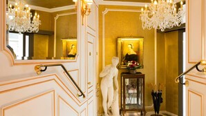 A luxurious interior with ornate gold paneling, a grand chandelier, and a statue of a woman. - Académie Hôtel Saint Germain (Paris)